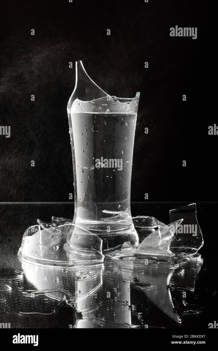 Studio beleuchtet gebrochenes Glas mit Wasser auf dem schwarzen Hintergrund isoliert gefüllt Stockfoto