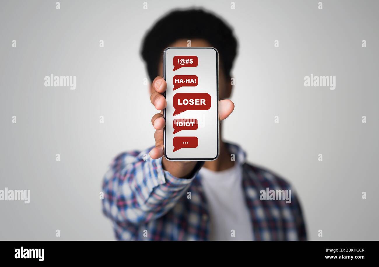 Cybermobbing-Konzept. Afroamerikanischer Kerl zeigt Smartphone mit missbräuchlichen Nachrichten auf dem Bildschirm. Collage Stockfoto