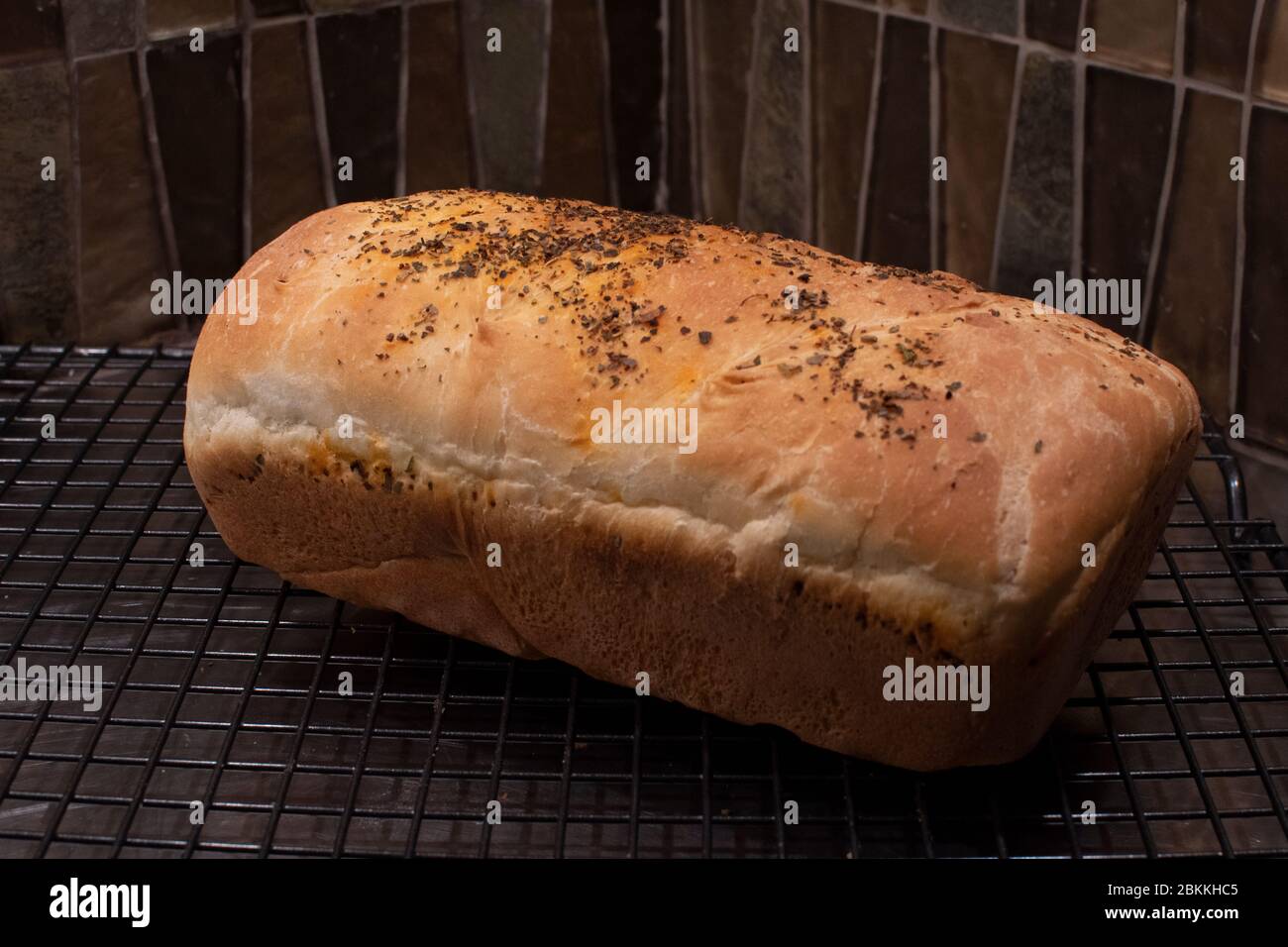 Ein Laib hausgemachtes Weißbrot, das mit Kräutern auf einem Drahtseil gekühlt wird Stockfoto