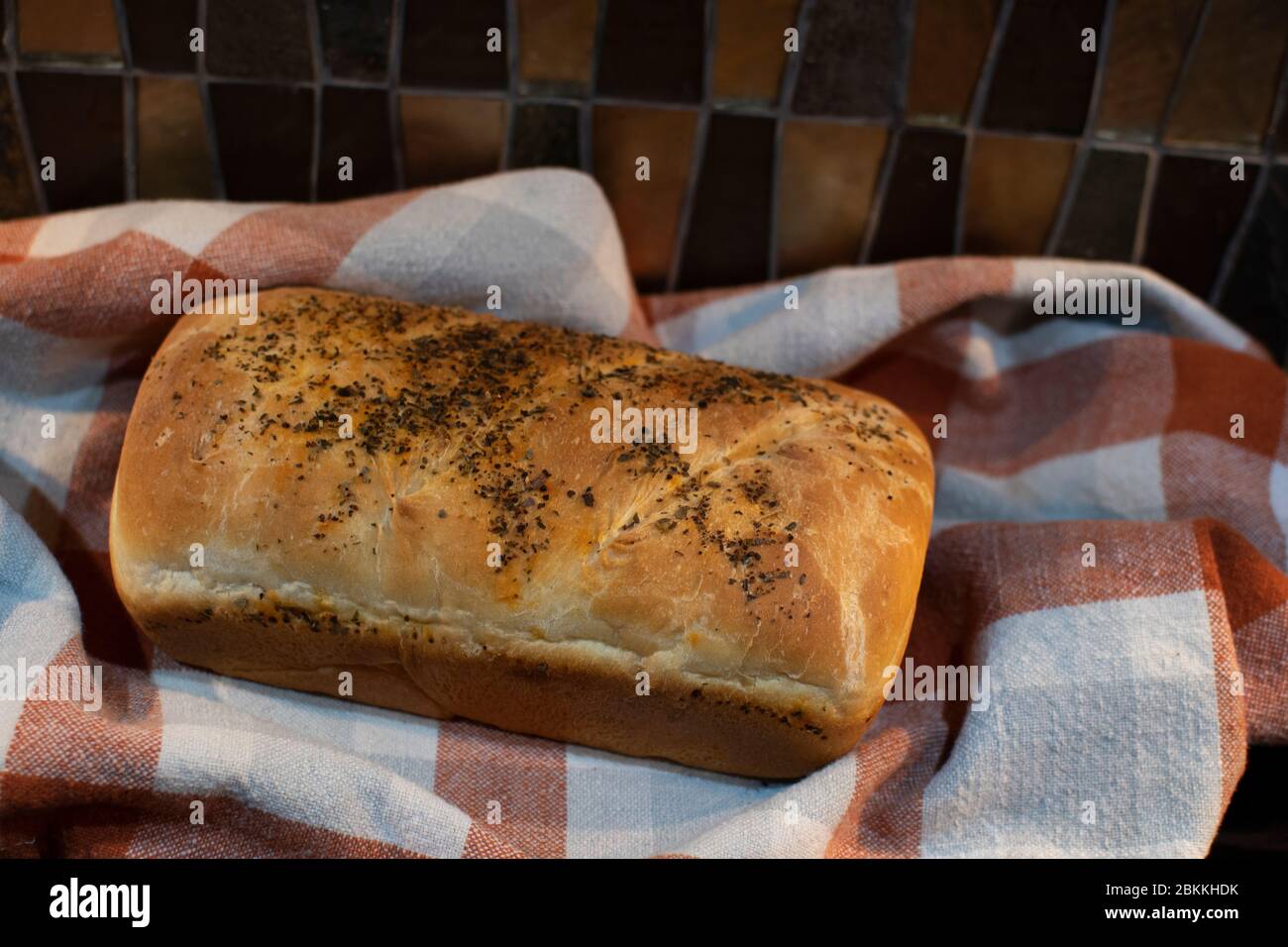 Frisch gebackenes Brot auf einem orange-grauen karierten Handtuch auf einer Küchentischfläche Stockfoto