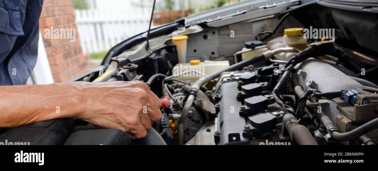 Mechaniker lehnt sich während einer Wartung unter der Motorhaube eines Autos, um nach Problemen mit dem Fahrzeug zu suchen und zu finden Stockfoto