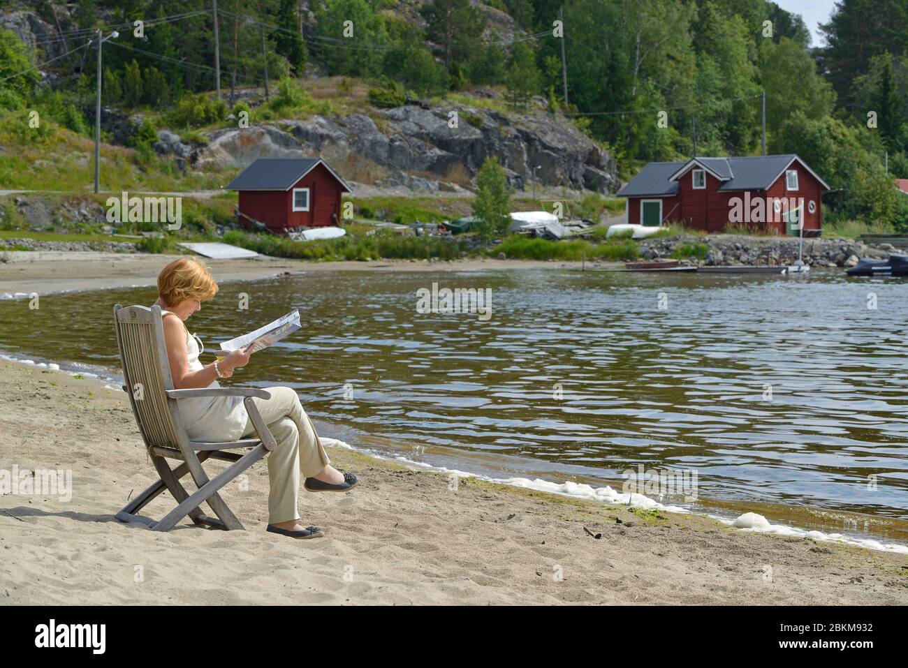 Eine Frau sitzt auf einem Liegestuhl am Strand, Alnö, Medelpad, Schweden Stockfoto