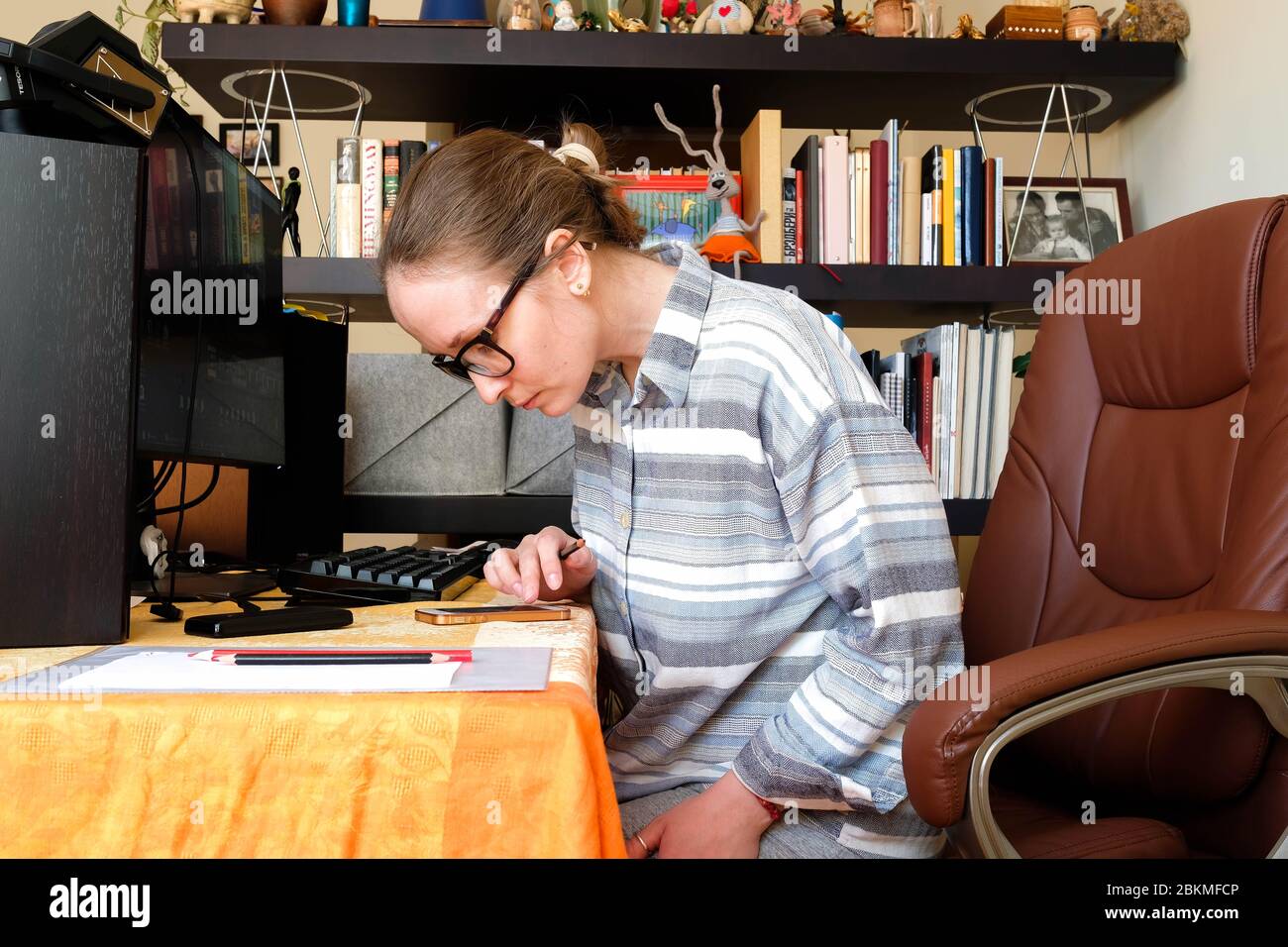 Eine Frau arbeitet zu Hause. Am Tisch sitzend, auf dem Telefon gebeugt. Gemütliche Atmosphäre, Wohnkleidung. Stockfoto