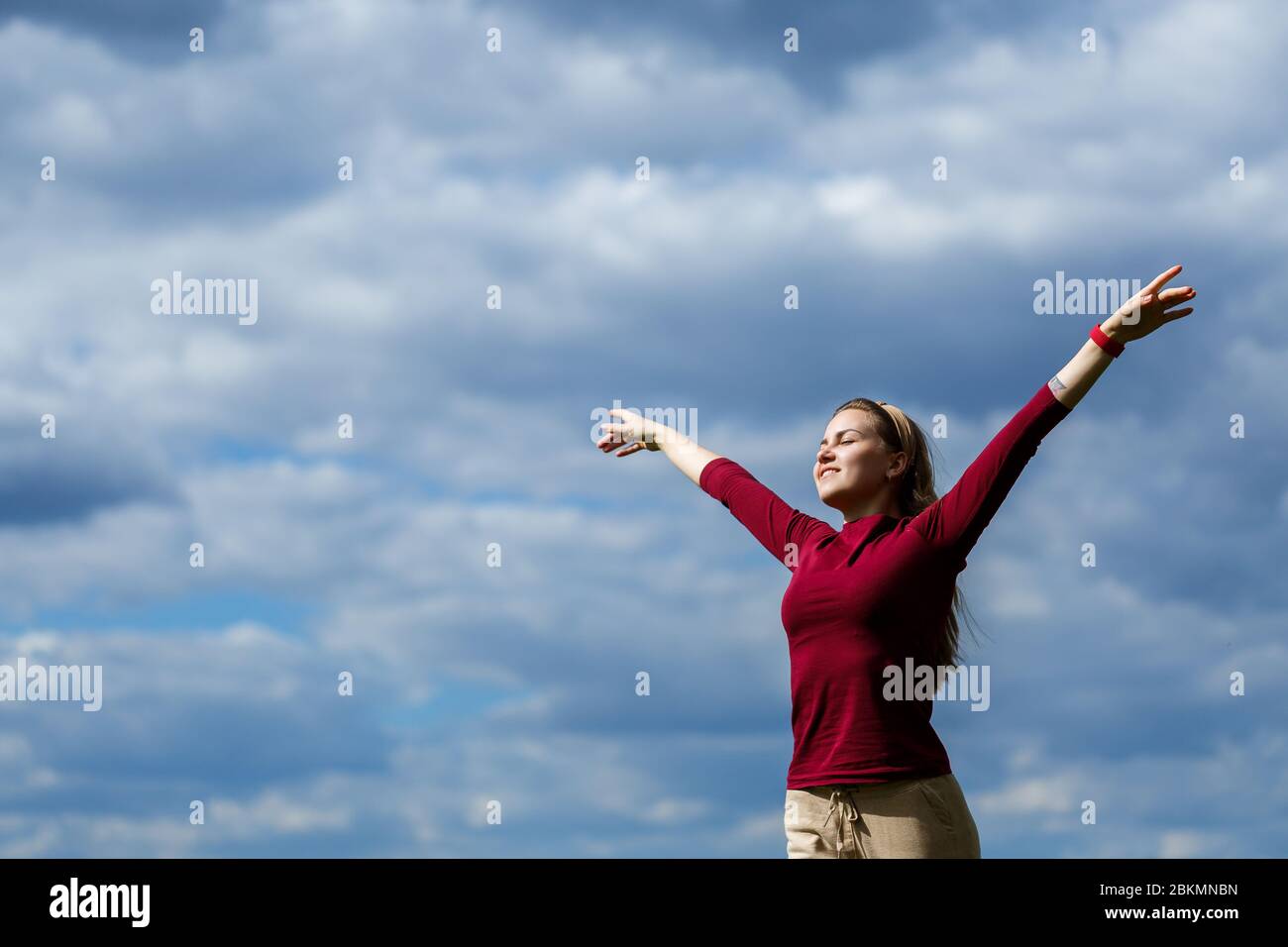 Freudiges junges Mädchen auf einem Hintergrund des Himmels mit Wolken. Er hob die Hände hoch und lachte. Glück im Lebensstil. Inspiration in der Natur. Ruhe nach Stockfoto
