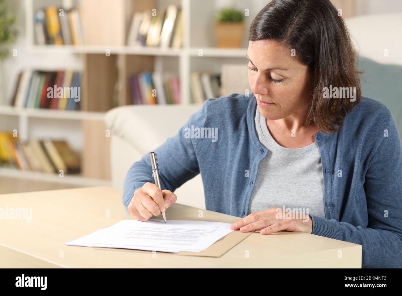 Seriöse Erwachsene Frau Unterschriftdokument auf dem Boden zu Hause sitzen Stockfoto