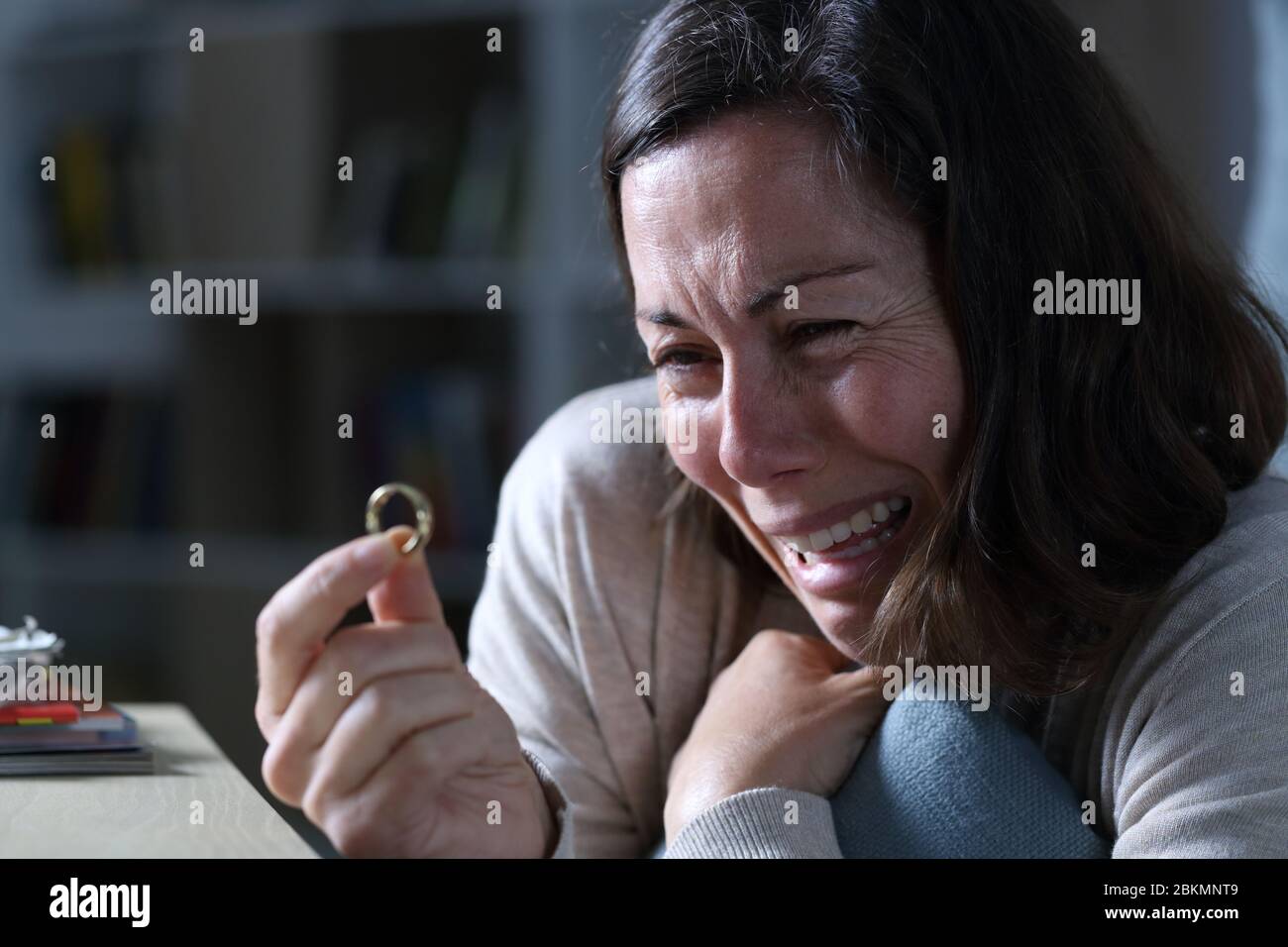 Traurige Frau weinend beim Blick auf Ehering, der in der Nacht zu Hause auf dem Boden sitzt Stockfoto