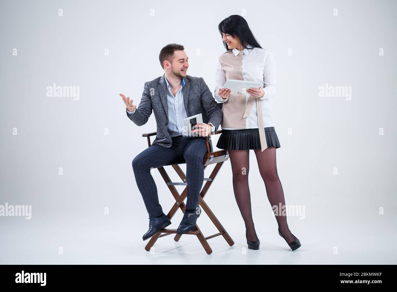 Ein erfolgreicher Mann in einem Anzug sitzt auf einem schwarzen Stuhl und eine Frau steht neben dem Blick auf die Tablets. Zukünftige Geschäftsleute lächeln und sprechen von einer ne Stockfoto