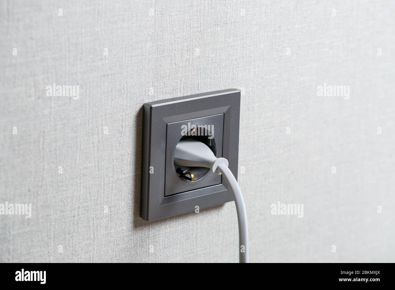Eine graue Steckdose an der Wand, die ein Gerät mit einem weißen Kabel enthält. Laden über eine Steckdose Stockfoto