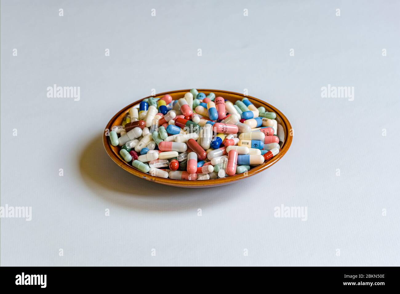 Ein kleiner Teller mit unterschiedlich farbigen medizinischen Kapseln, auf einem weißen Tisch angezeigt gefüllt Stockfoto