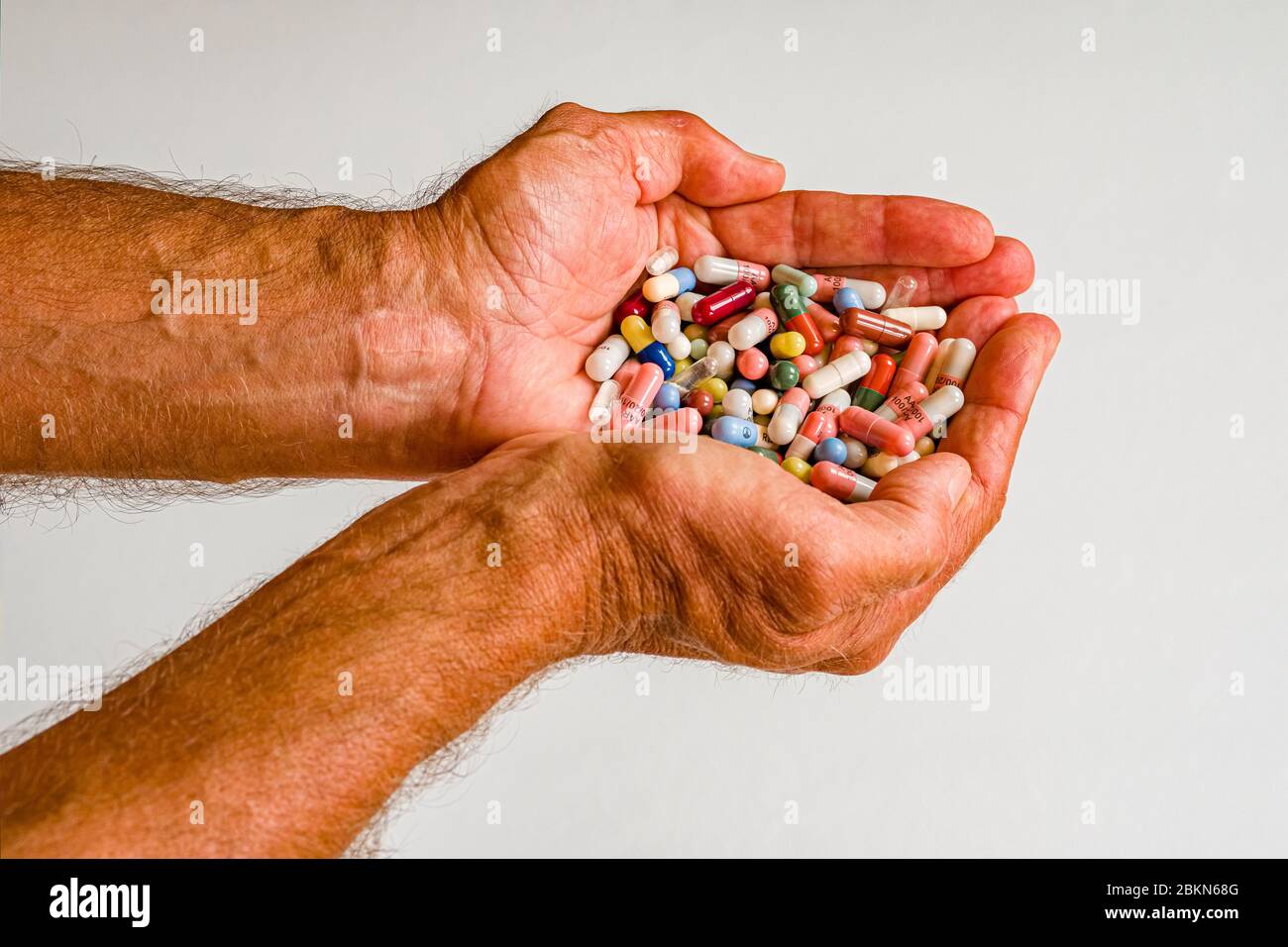 Ein Paar männliche Hände, gefaltet als Schale, gefüllt mit unterschiedlich farbigen medizinischen Kapseln, auf einem weißen Tisch ausgestellt Stockfoto