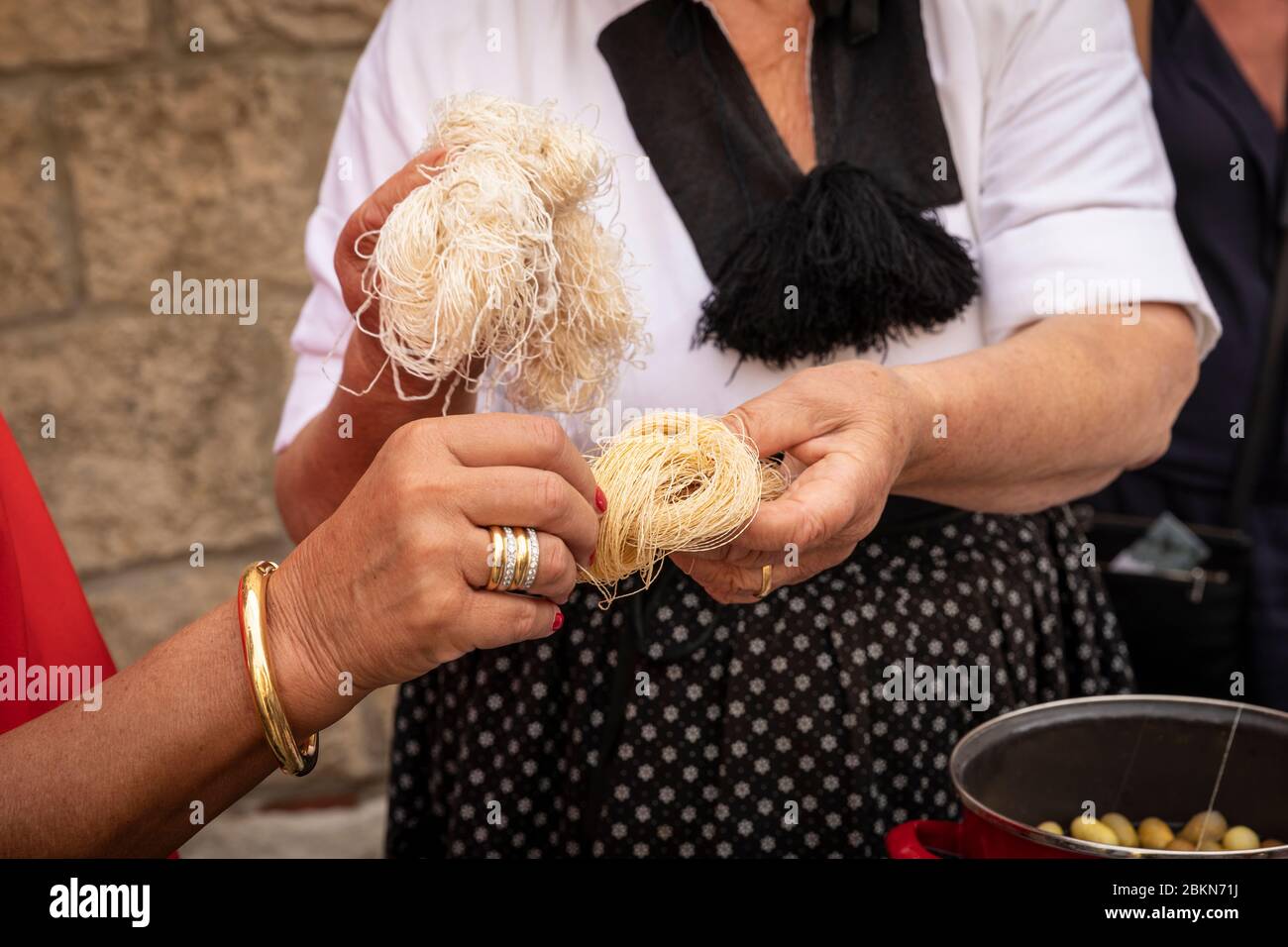 Eine Frau, die ein tranditional altes Folklore-Kostüm trägt, das den Menschen zeigt, wie Seidengarn in einer rustikalen authentischen Umgebung hergestellt wird Stockfoto