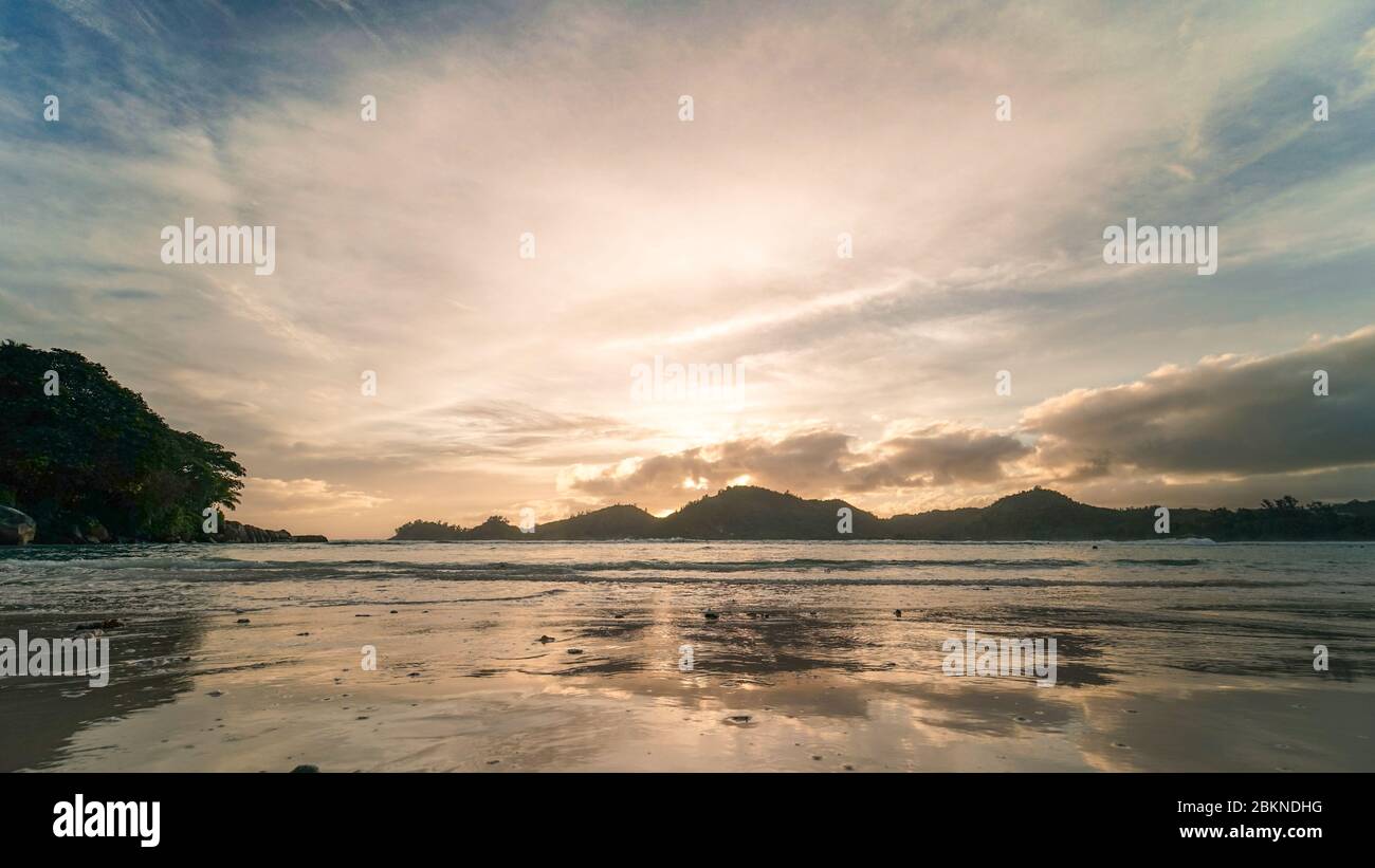 Sonnenuntergang auf den Seychellen mit ruhigem Indischen Ozean, der die Reflexion des Sonnenuntergangs am nassen Sandstrand zeigt Stockfoto