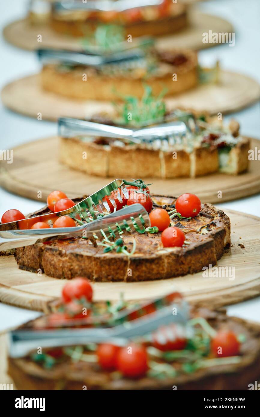 Die Pasteten mit Kirschtomaten und grünen Keimen liegen auf runden Holzschalen und in Scheiben mit Zange geschnitten Stockfoto