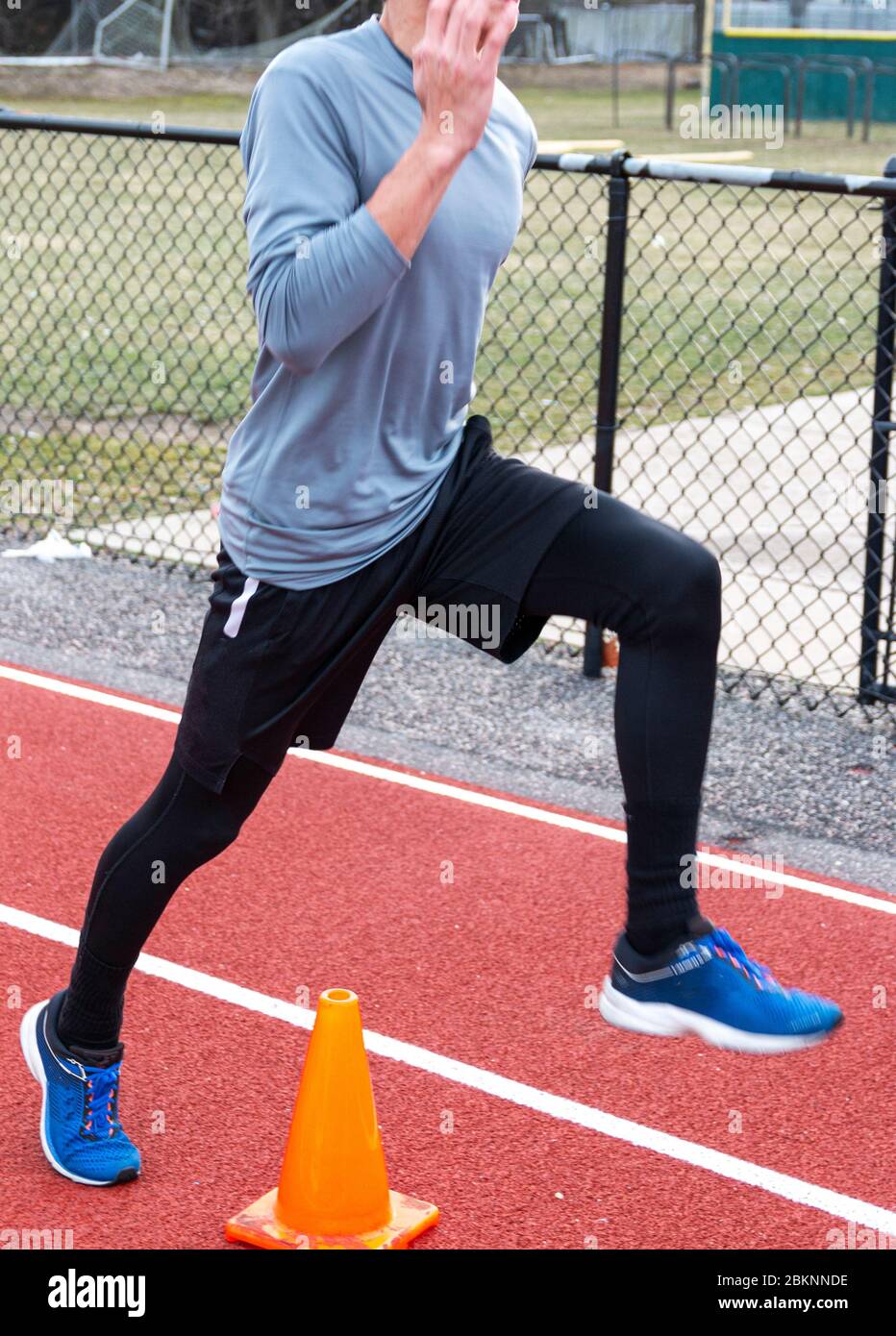 Ein High School Sprinter läuft über einen orangefarbenen Kegel lernen, um sein Bein höher aus dem Boden beim Rennen. Stockfoto