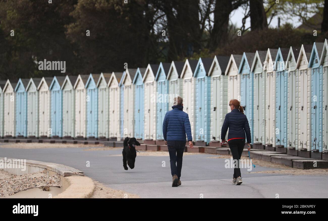 Menschen laufen ihren Hund an Strandhütten am Avon Strand in Christchurch, Dorset vorbei. Stockfoto