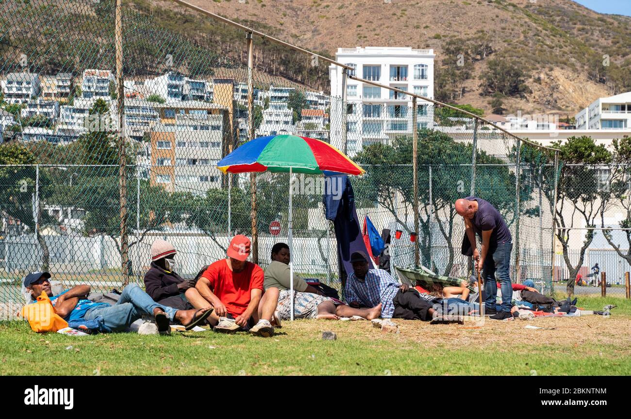 Südafrika tritt am 26. April 2020 in eine landesweite Sperrung des Coronavirus ein. Obdachlose versammeln sich vor einem Tennisplatz in Sea Point Kapstadt. Stockfoto