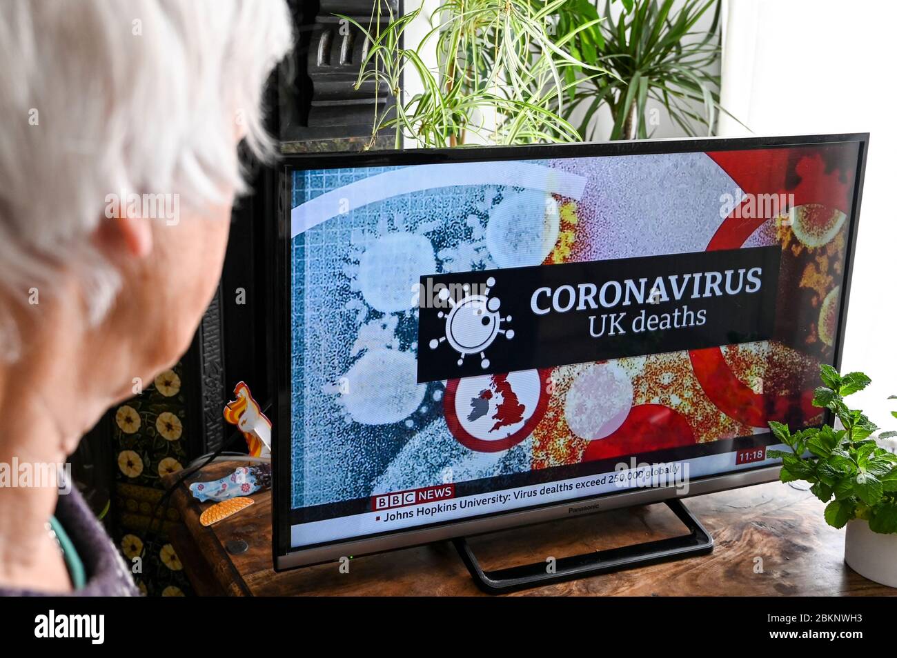 Coronavirus-Grafik in Fernsehnachrichten, die die Todesraten in Großbritannien und weltweit ankündigt, die von einem älteren Zuschauer beobachtet werden. Stockfoto