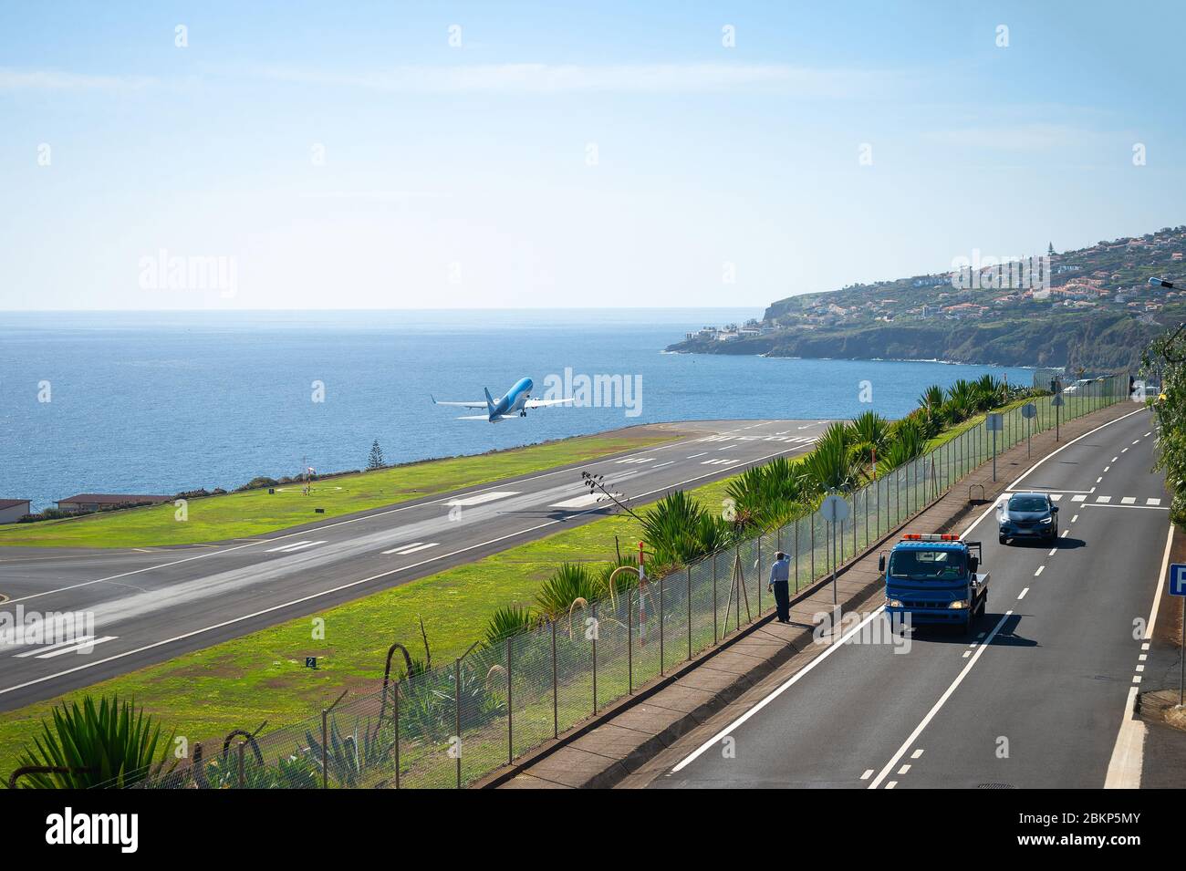 Mann beobachtet Flugzeug, das von der Start- und Landebahn des internationalen Flughafens Funchal abfährt, landschaftlich schönen Blick aufs Meer und die Stadt im Hintergrund, Autos auf der Autobahn, Madeira, Stockfoto