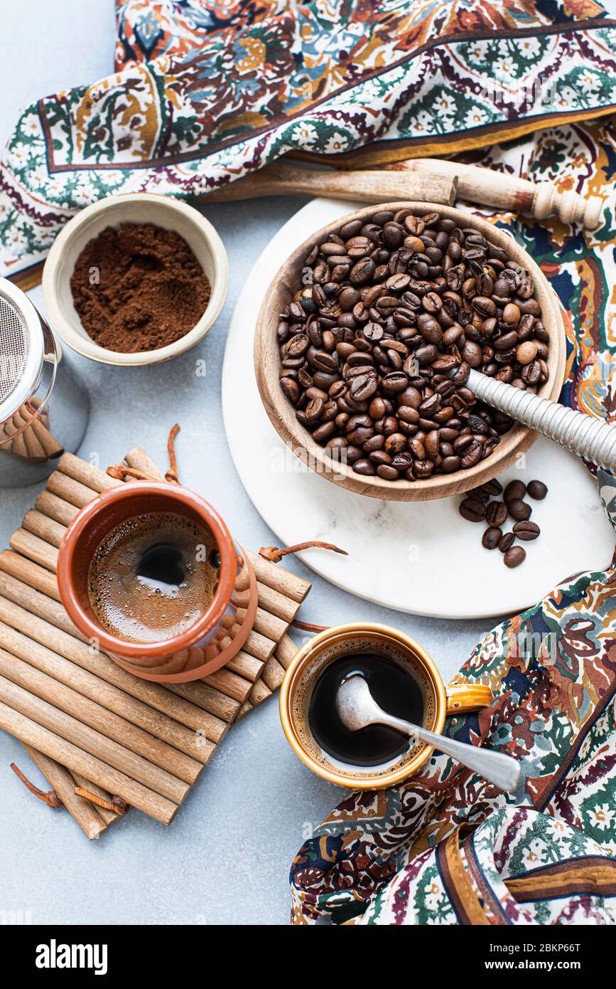 Blick von oben auf eine Schüssel mit Kaffeebohnen, neben gemahlenem Kaffee, eine Tasse Kaffee und einen gemusterten Schal. Stockfoto