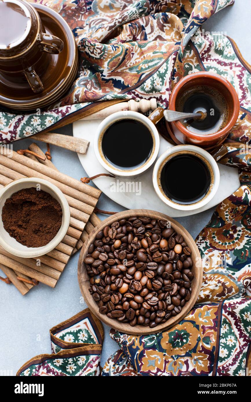 Blick von oben auf eine Schüssel mit Kaffeebohnen, neben gemahlenem Kaffee, eine Tasse Kaffee und einen gemusterten Schal. Stockfoto