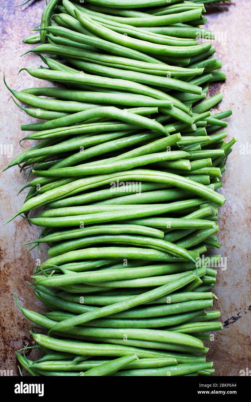Grüne französische Bohnen mit Stielen, die in einem langen Stapel auf einer grauen Oberfläche entfernt wurden. Stockfoto