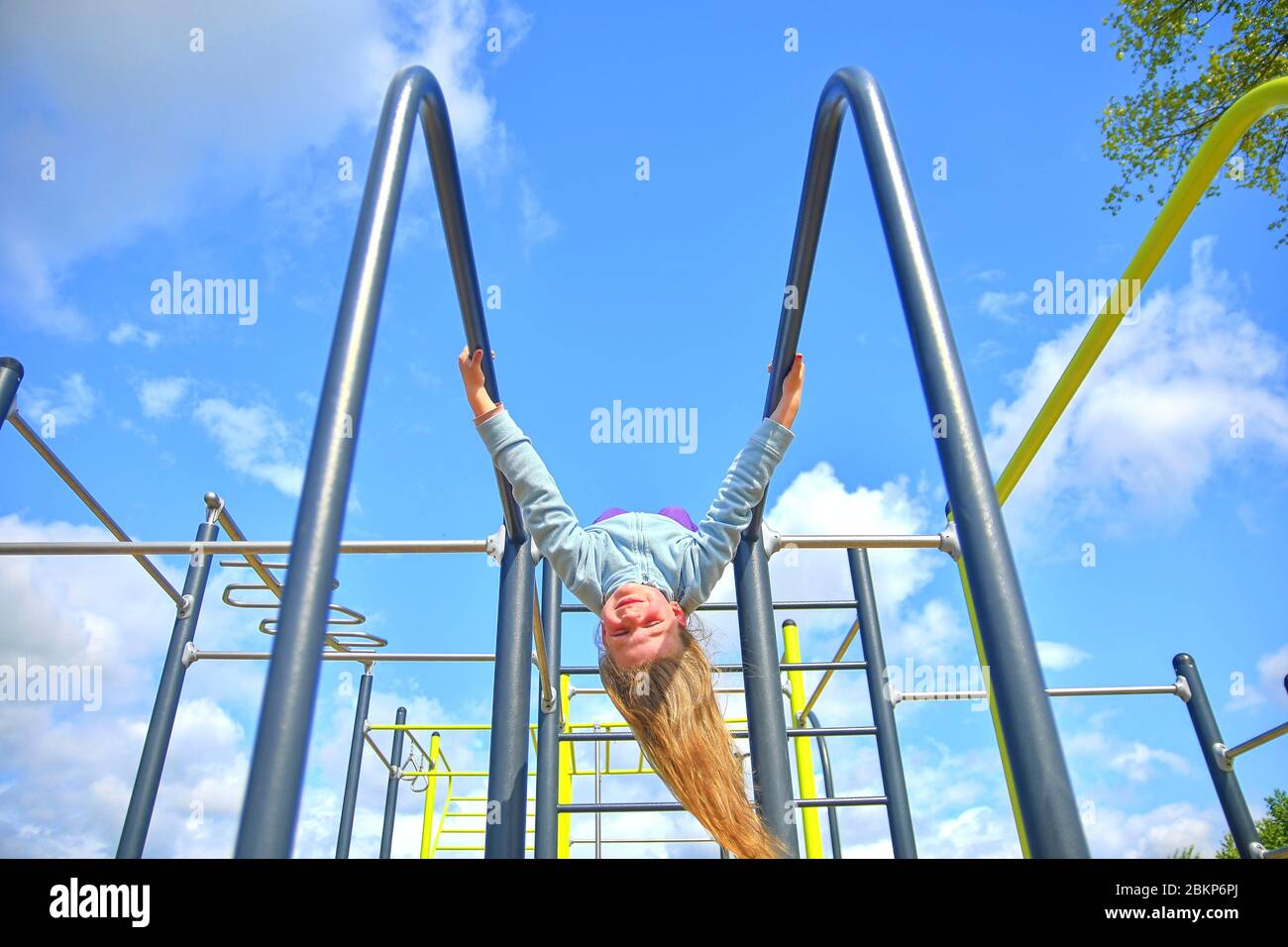 Liebenswert kleines Mädchen lachen glücklich, hängend kopfüber auf parallelen Bars auf dem Spielplatz. Stockfoto