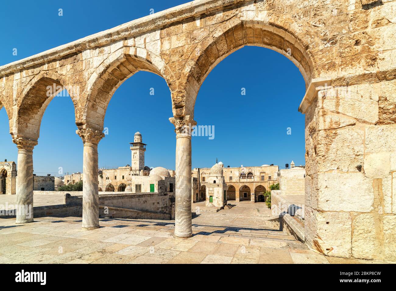 Blick auf typische Häuser und Minarett unter blauem Himmel durch alte Steinbögen auf dem Tempelberg in der Altstadt von Jerusalem, Israel. Stockfoto