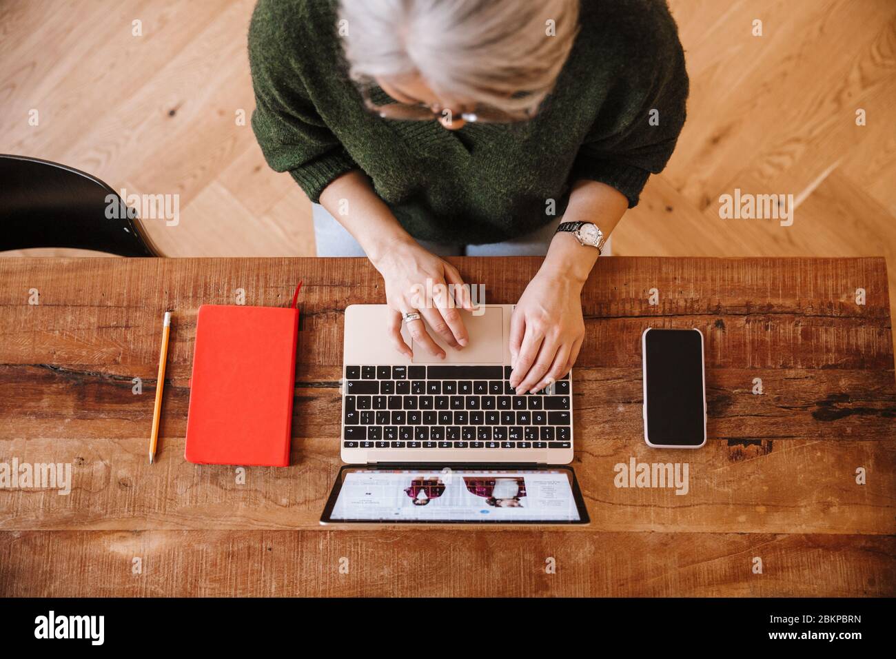 Foto von silbernen reifen Frau in Brillen mit Laptop während am Tisch im Wohnzimmer sitzen Stockfoto