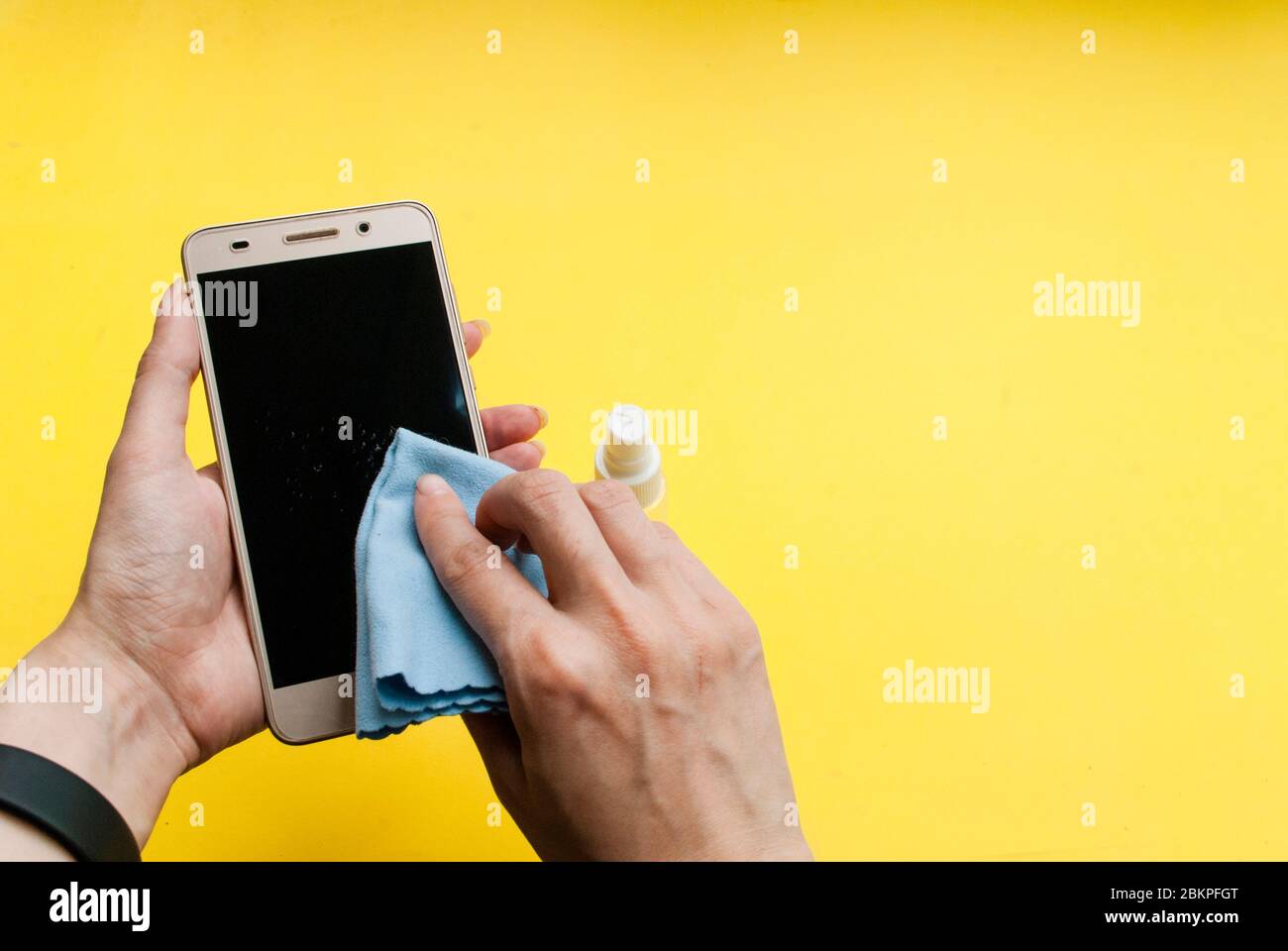 Junge Frau wischt ein Telefon mit einem antiseptischen, gelben Hintergrund Ort für Text Stockfoto