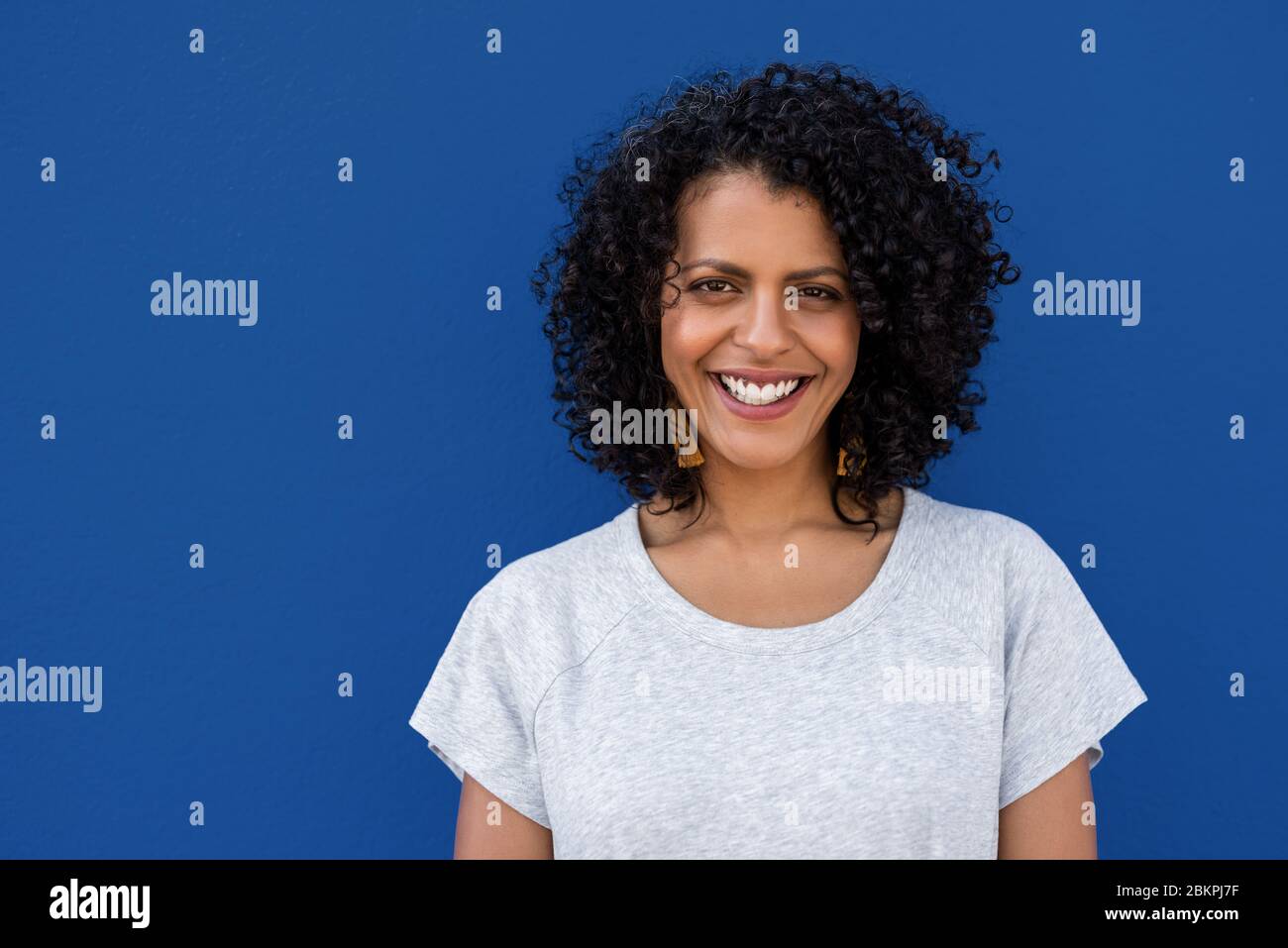 Lächelnde junge Frau steht vor einem bunten blauen Hintergrund Stockfoto