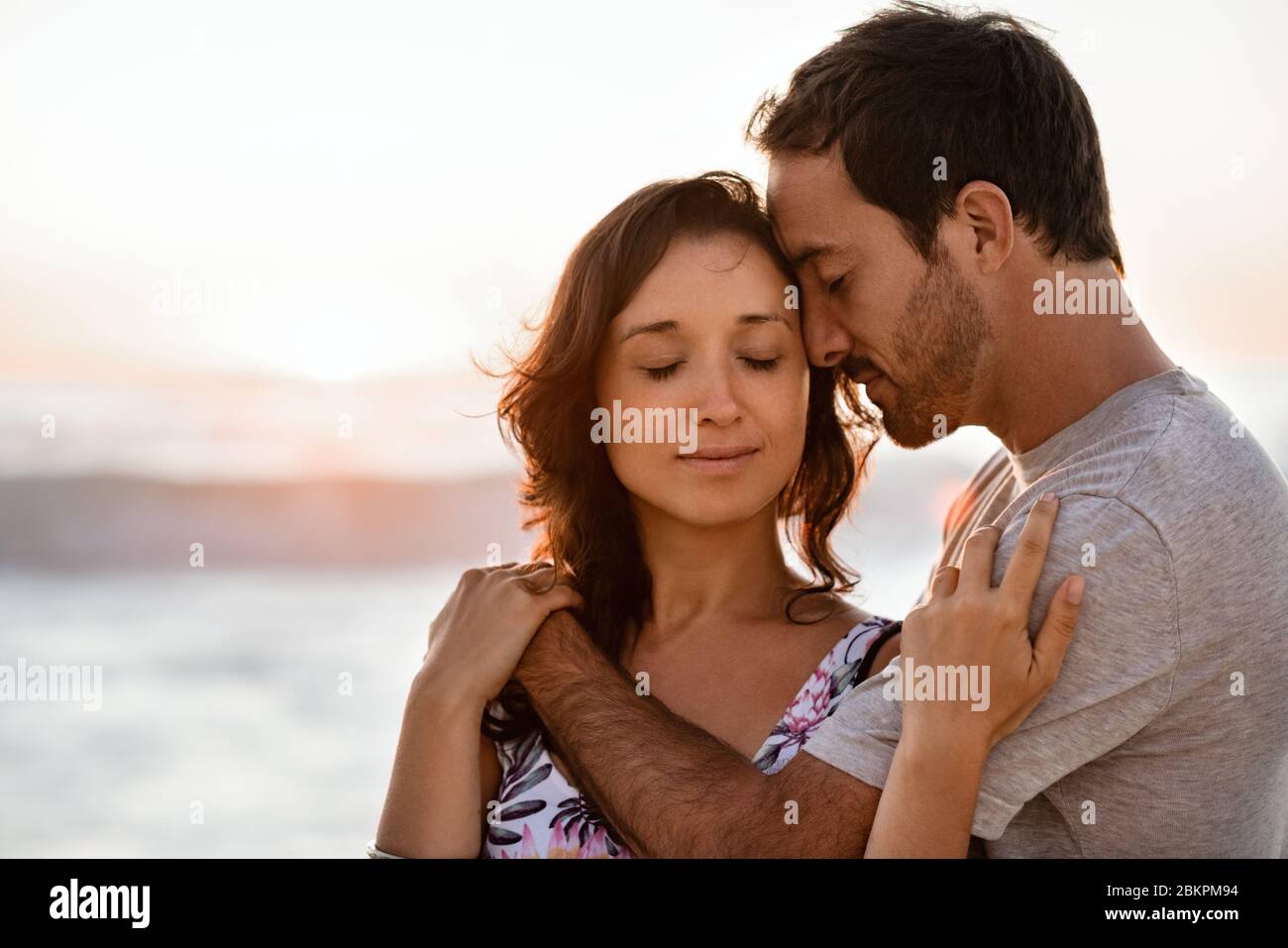 Liebevolles junges Paar, das in der Abenddämmerung am Strand zusammensteht Stockfoto