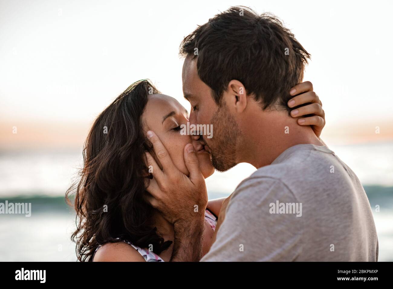 Liebende Paare teilen sich einen Kuss an einem Strand in der Dämmerung Stockfoto