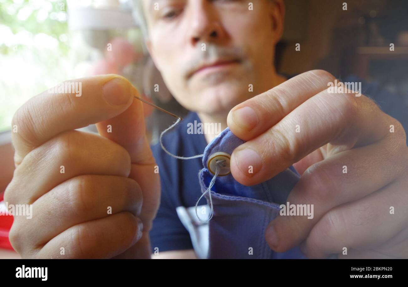 Schneidermann mit Nadel und Faden in der Hand. Handgefertigte Arbeit. Manuelles Nähen auf den Hemdknopf. Heimwerkerhandwerk. Stockfoto