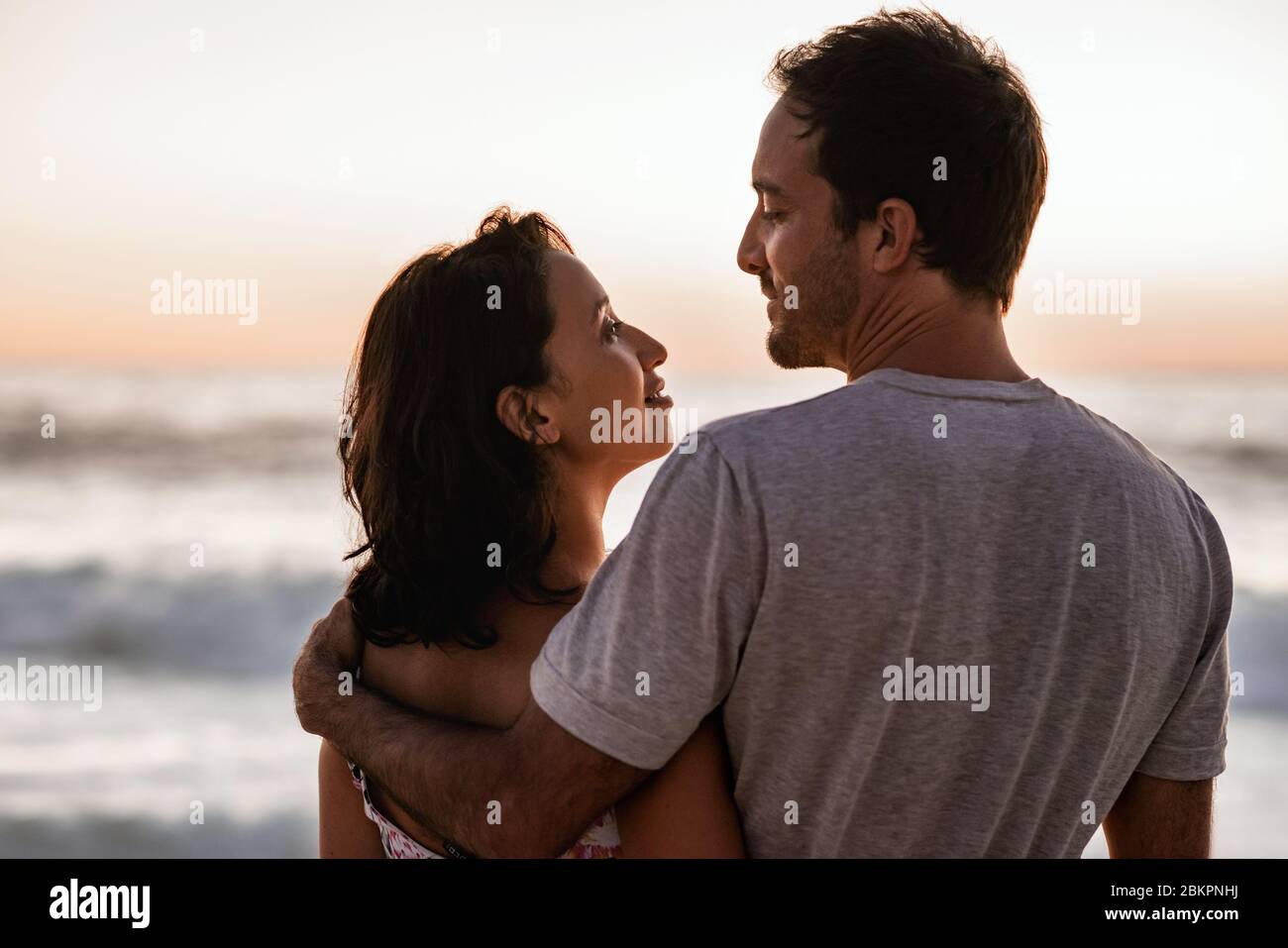 Liebende junge Paare, die einen Sonnenuntergang über dem Meer beobachten Stockfoto