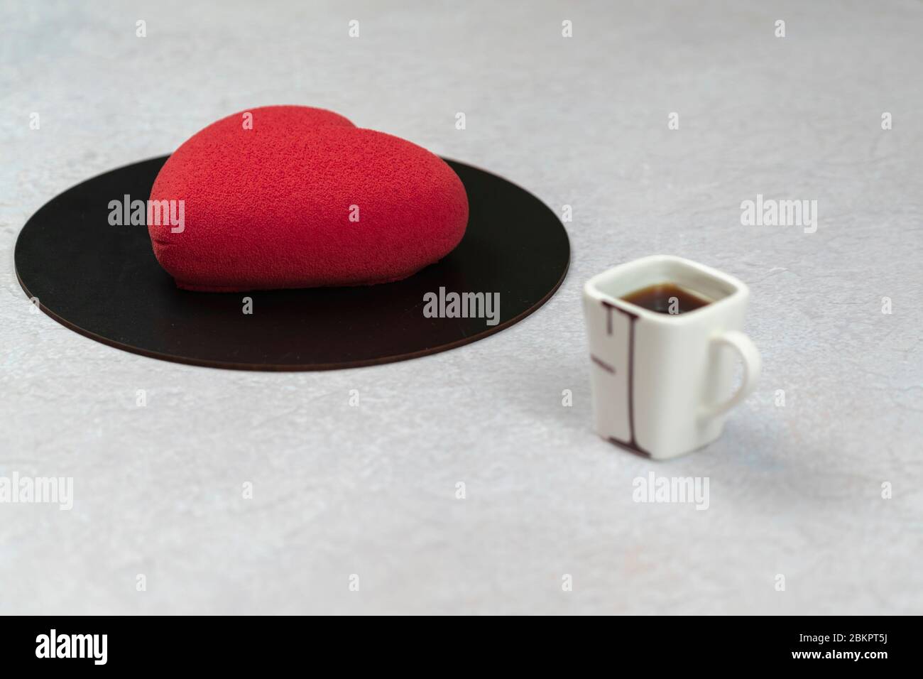 Velours Kuchen in Form eines Herzens und einer Tasse Kaffee, Nahaufnahme. Moderne französische Mousse Gebäck Dessert mit Schokolade Velour.Konzept der Süßwaren Stockfoto