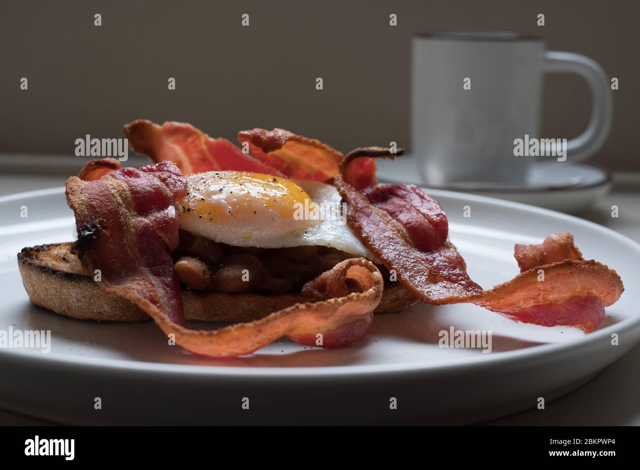 Warmes britisches Frühstück mit Ei, Speck und hausgemachten Bohnen auf Sauerteig Toast Stockfoto
