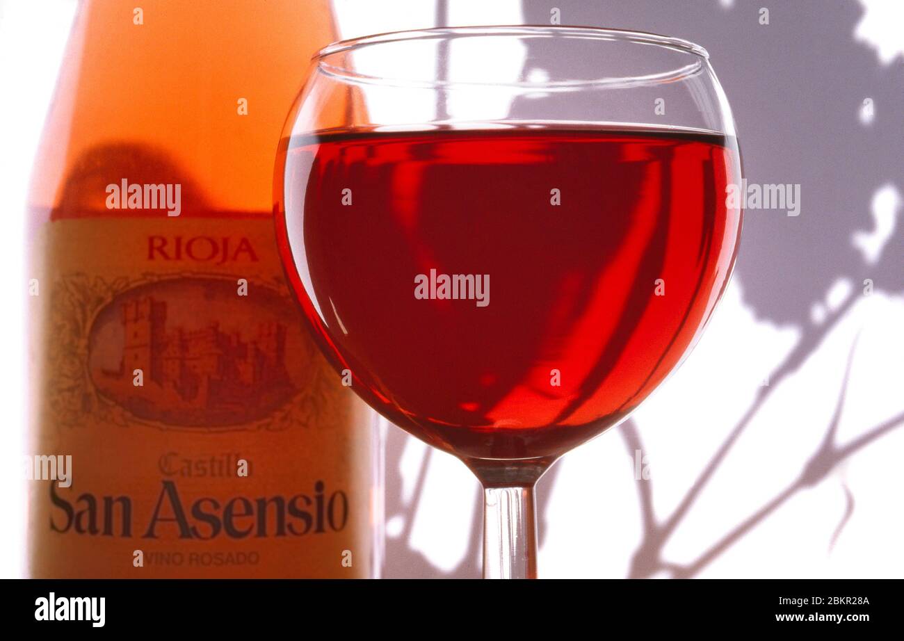 Rosé Spanisches Weinglas und Flasche San Asensio Rioja Alfresco, mit weißer Wand hinter und Schatten der nationalen Blume, die Nelke. Stockfoto