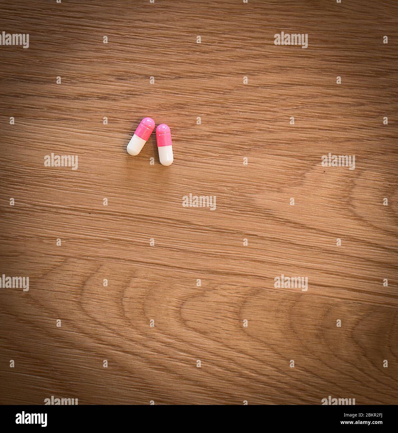 2 rosa und weiße Ibuprofen Kapseln auf einem Holztisch sitzen Stockfoto