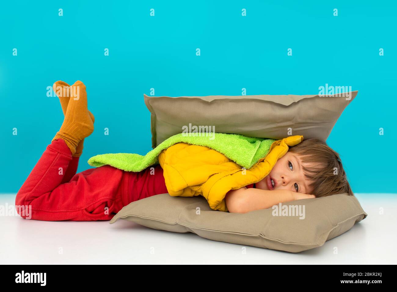 Junge versteckt in Kissen auf blauem Hintergrund Stockfoto