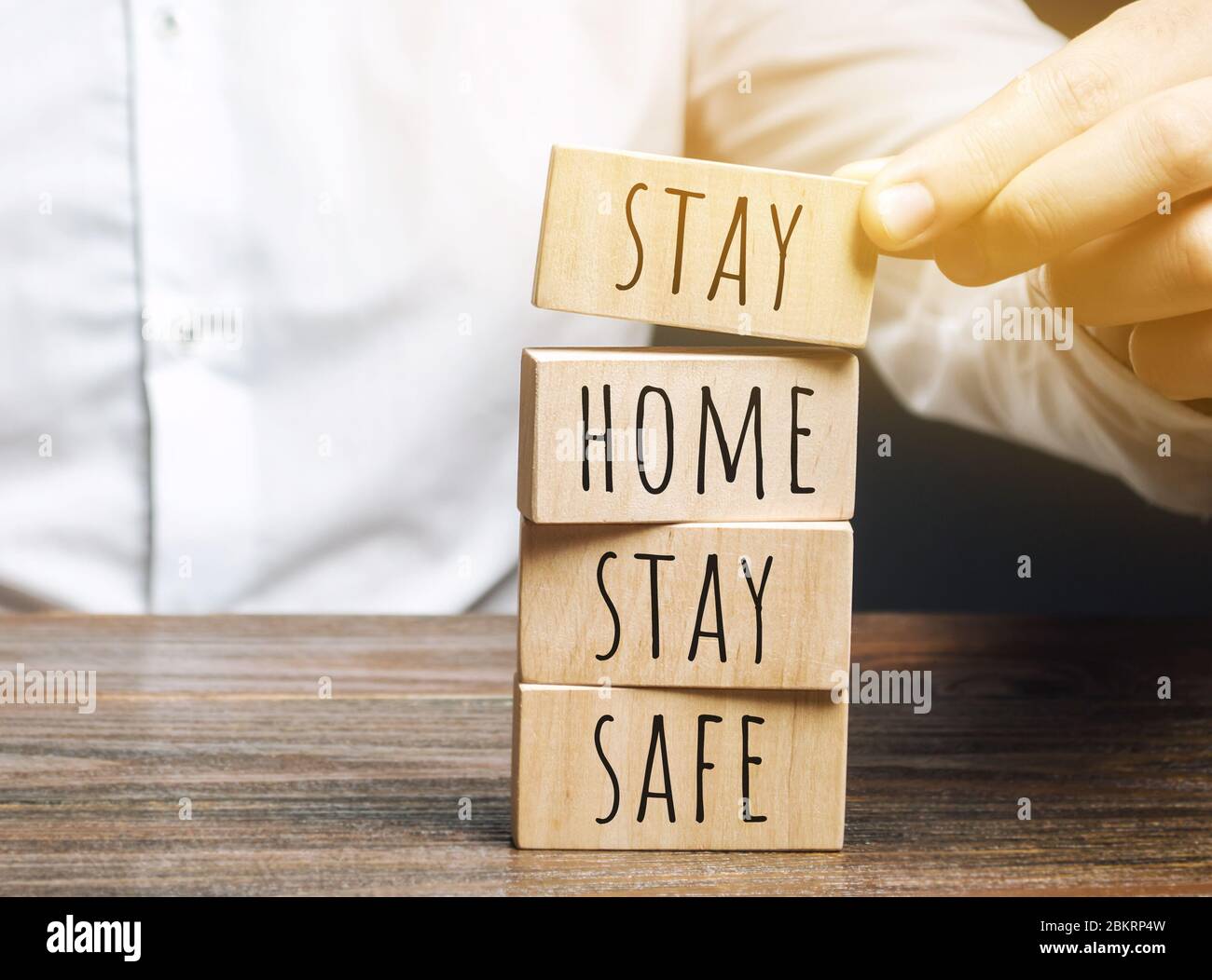 Mann setzt Holzblöcke mit den Worten zu Hause bleiben sicher. Das Konzept der Prävention von Coronavirus-Infektion. Selbstisolierung und Quarantäne. COVID- Stockfoto
