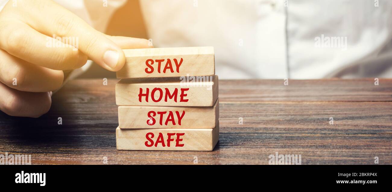Mann setzt Holzblöcke mit den Worten zu Hause bleiben sicher. Das Konzept der Prävention von Coronavirus-Infektion. Selbstisolierung und Quarantäne. COVID- Stockfoto