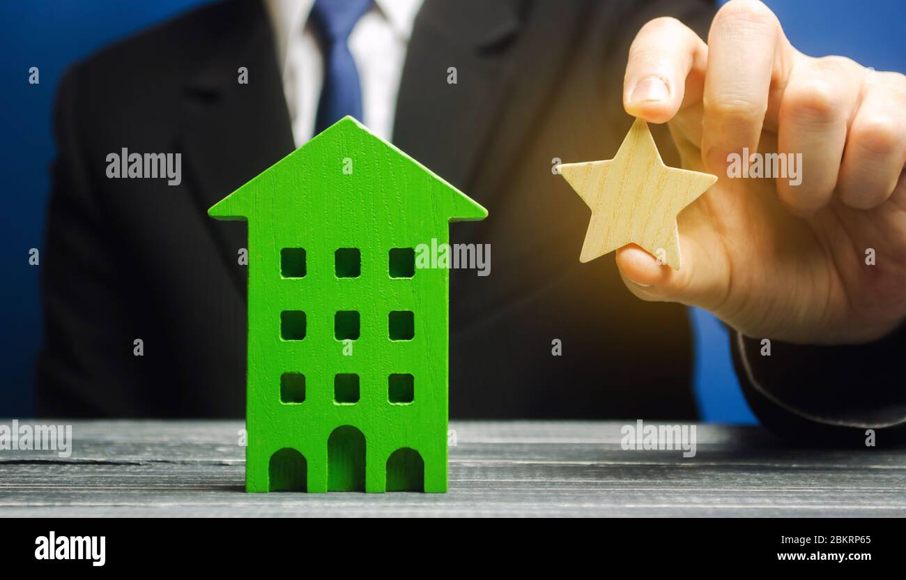 Geschäftsmann hält einen Stern in der Nähe des Hauses. Das Konzept, von einem Hotel einen Stern zu bekommen. Verbesserung der Servicequalität. Kritik und Bewertung. R Stockfoto