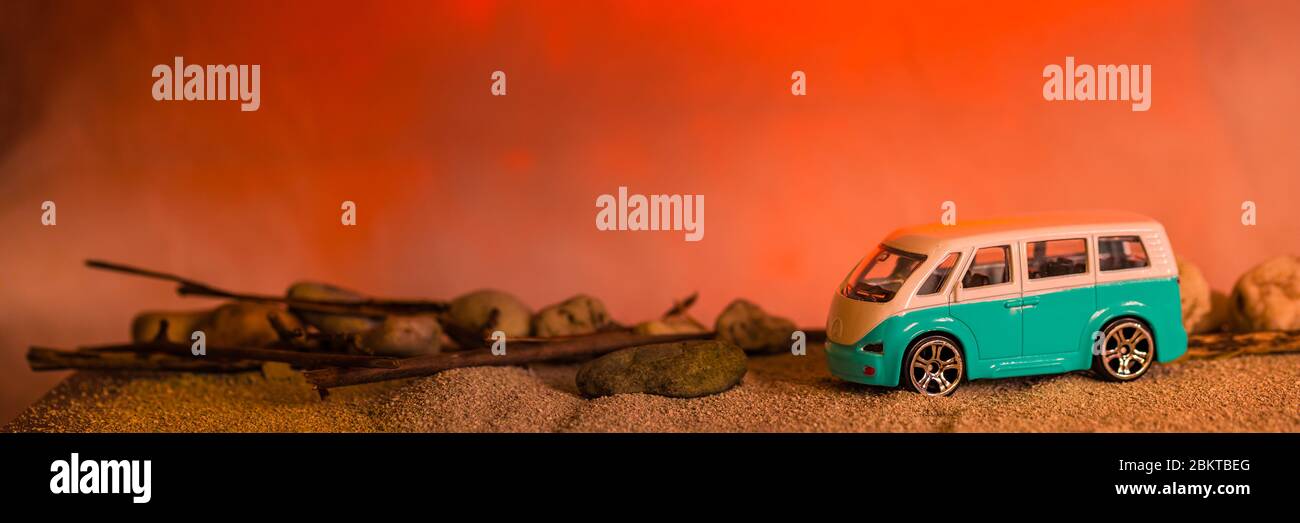 Ein kleines blaues Wohnmobil schilhouettiert gegen eine dramatische Sonneneinlage am Strand Stockfoto