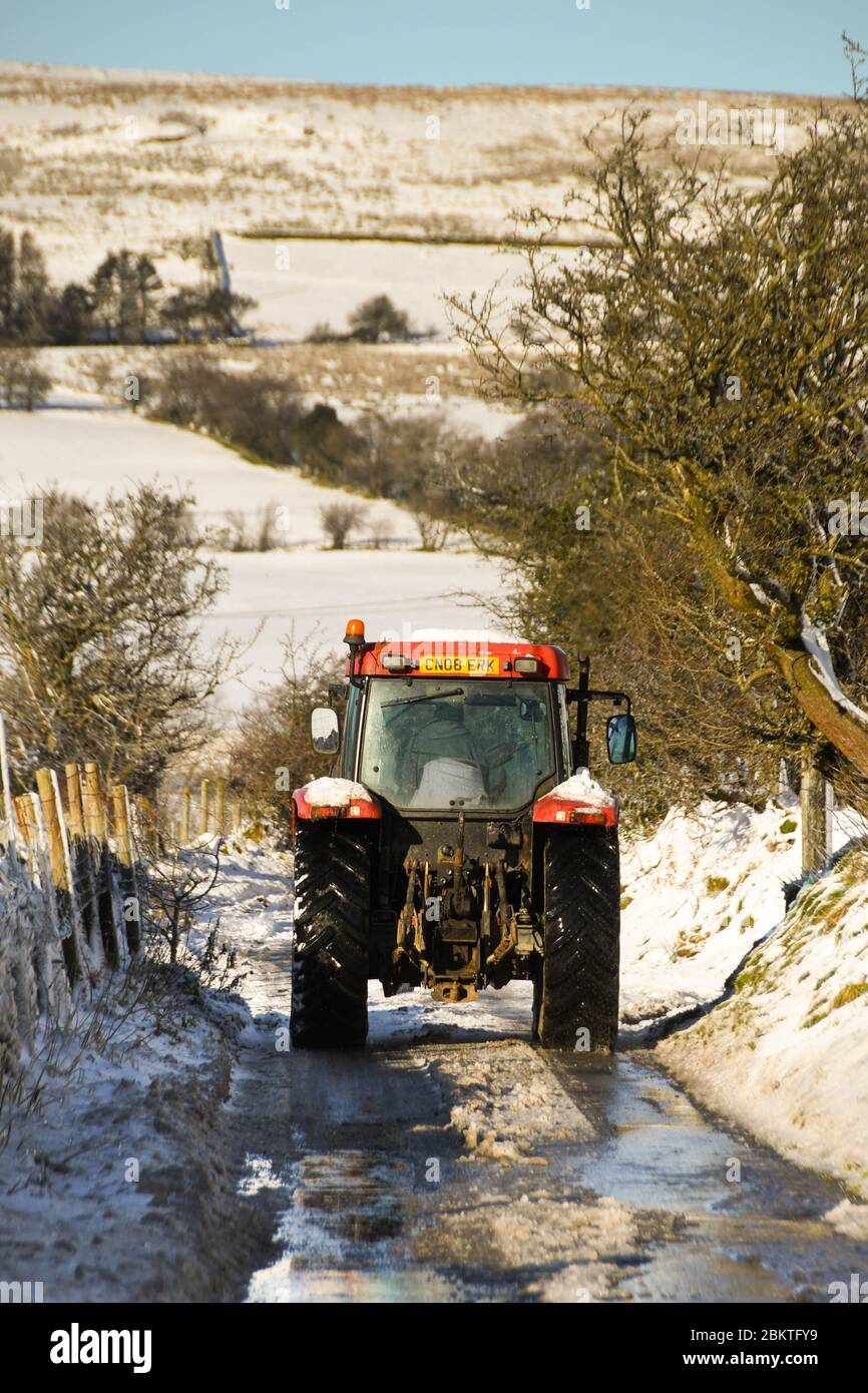 Pontypridd, Wales - Dezember 2017: Bauernhof Traktor fahren auf einer schneebedeckten Landstraße im Winter Stockfoto