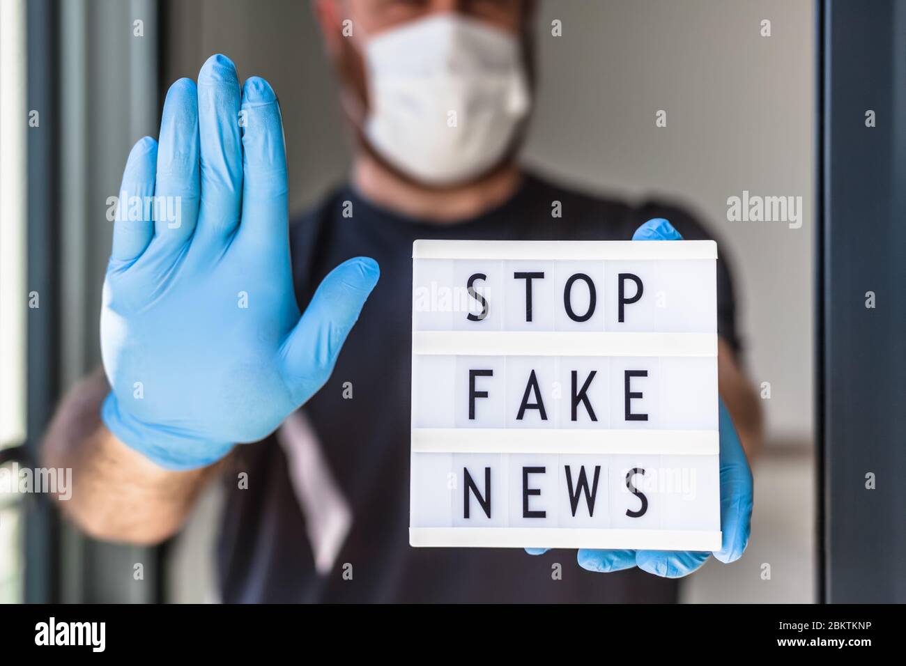 Fake News Infosemics during Covid-19 Pandemie Concept. Mann trägt Schutzmaske und medizinische Handschuhe an den Händen halten Leuchtkasten mit Text Stop Fake ne ne Stockfoto