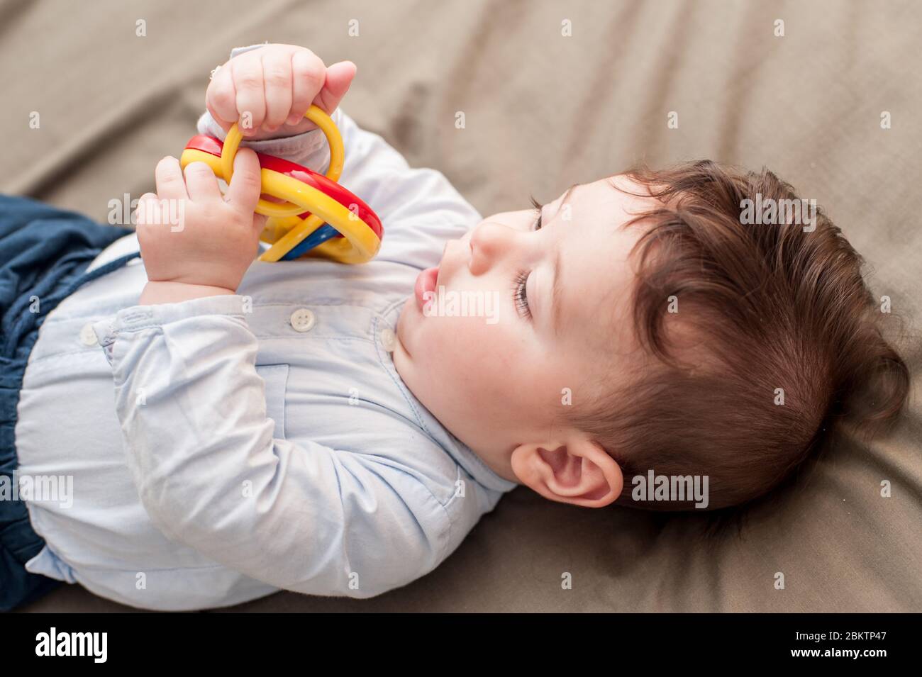 Blick aus dem hohen Winkel eines niedlichen kaukasischen Jungen, der im Bett liegt und ein Spielzeug hält. Stockfoto