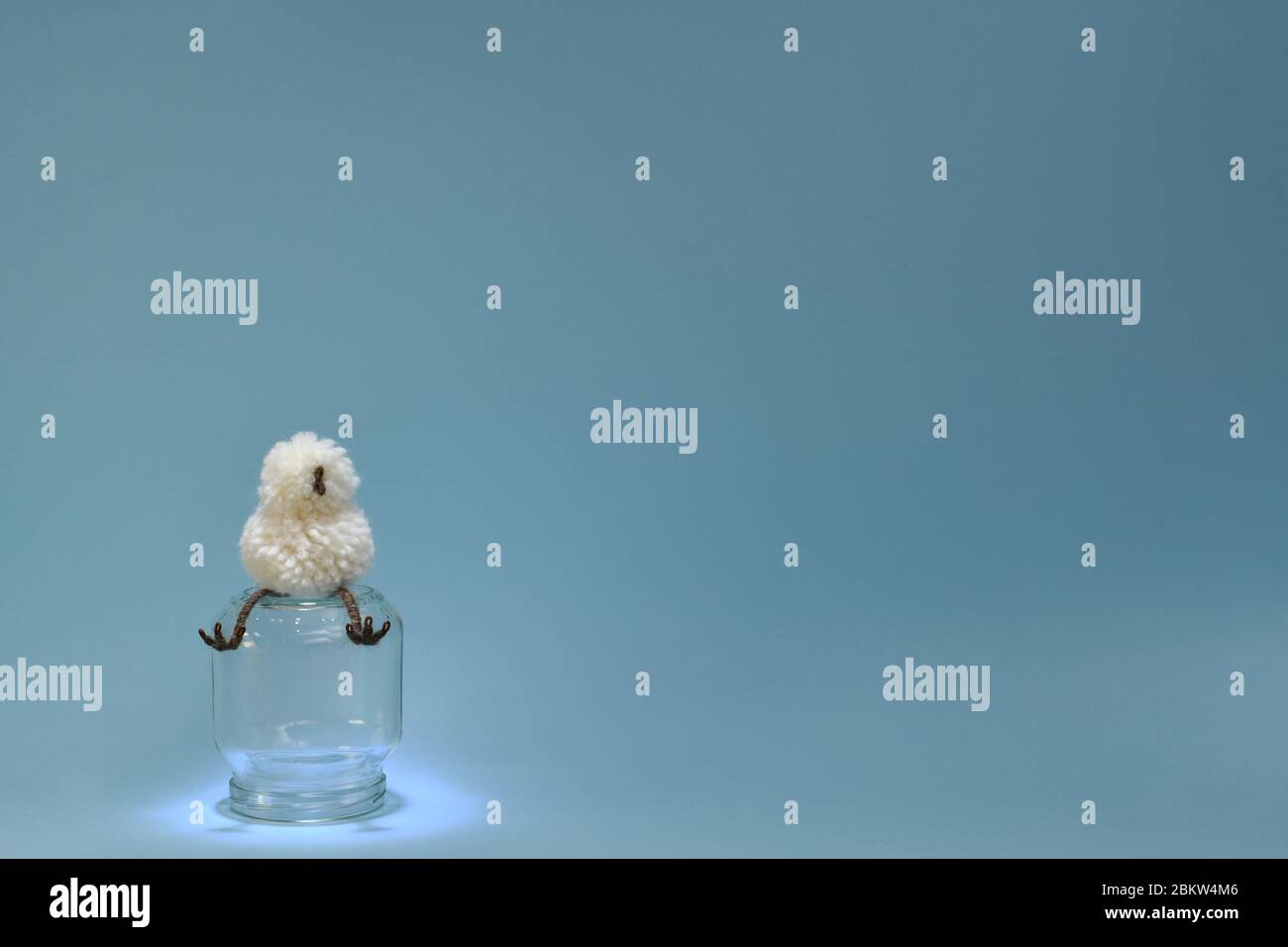 Ein Spielzeug Küken eines Hühners sitzt isoliert auf einem Glas Tank hängenden Pfoten. Stockfoto