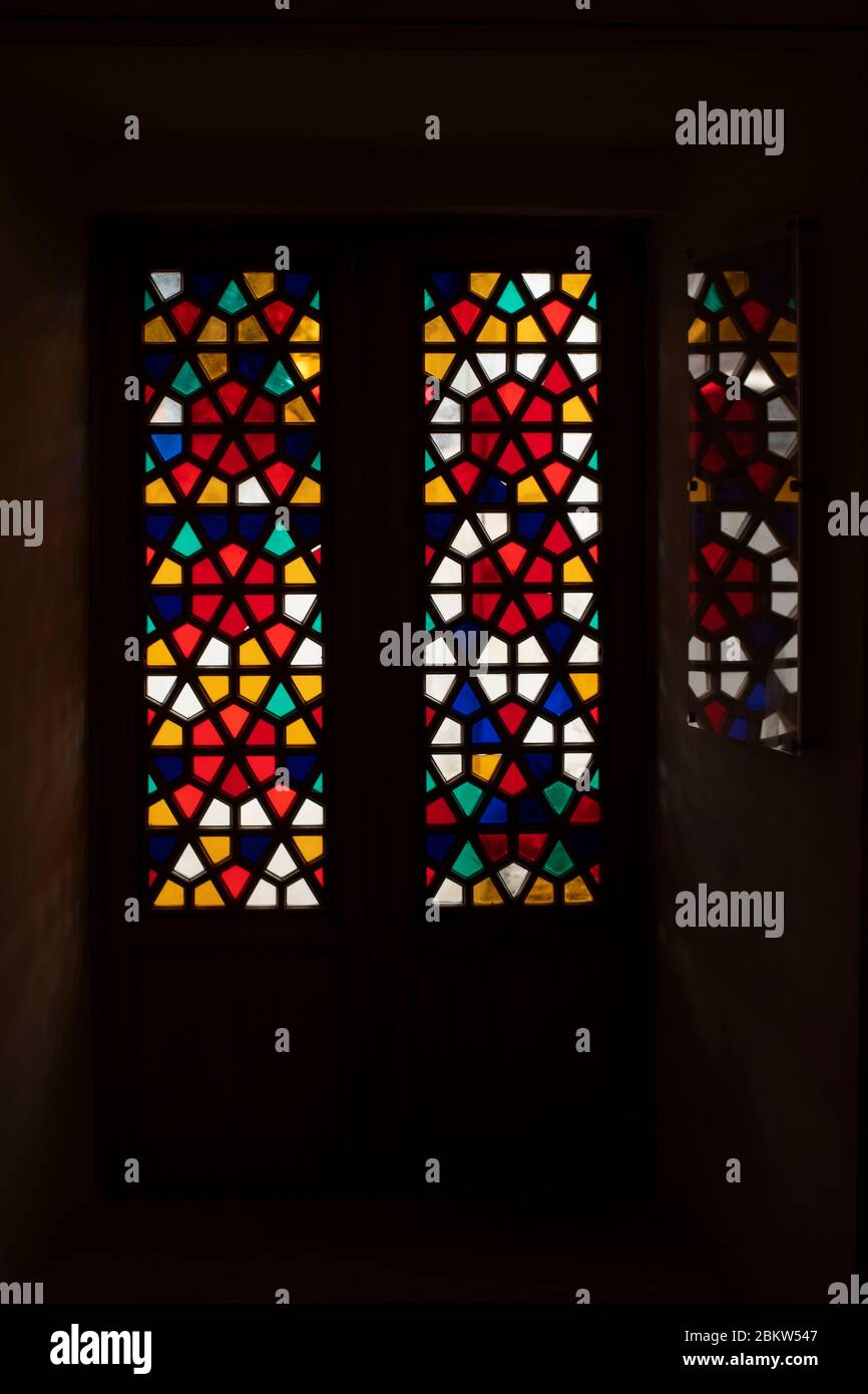 Eine Tür aus Buntglas-farbigem Glas. Das Muster spiegelt sich auf dem Glas. Das Foto ist dunkel und wirkt einschüchternd. Das Muster auf dem Buntglasfenster besteht aus vielen Fünfecken. Stockfoto