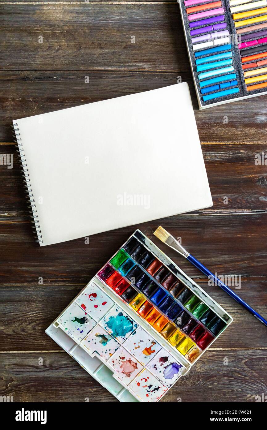 Flacher Kunstarbeitsplatz, Holztisch mit Pinsel, Aquarellfarben, Papier Canva und Kreide Pastellkreiden Stockfoto