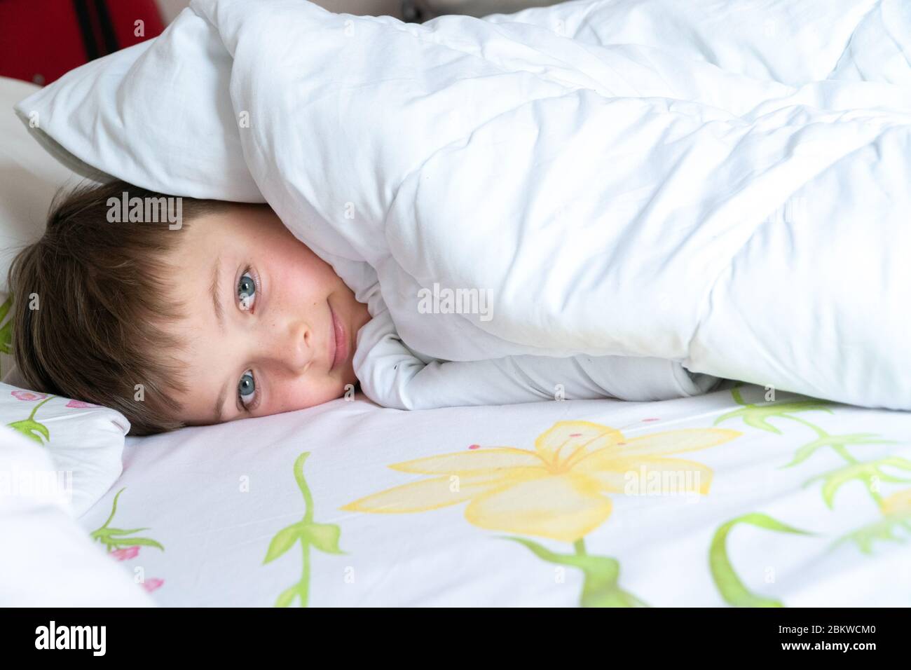 Draufsicht des kleinen Jungen im Bett, der sein Gesicht mit einer weißen Decke oder einem Deckblatt bedeckt. Schlafender Junge. Stockfoto